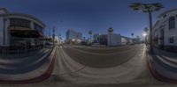 a street with buildings, palm trees and the moon on a sunny day taken from a fish eye lens