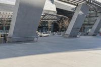 a walkway near an office building is shown, with steel poles in the middle and concrete panels that form the ceiling