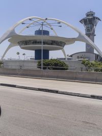 traffic moves down the freeway near an airport control tower and air traffic clock with other buildings in the background