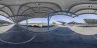 a fisheye image of an outdoor area with concrete flooring, and blue metal arches