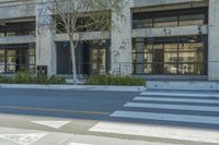 a person sitting on a bench by a cross walk in the shade of an office building