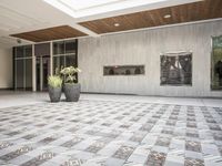 a tiled floor outside of a building near pots of planties on each side of the room