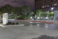 an empty parking lot lit up at night with lights on and trees in the background