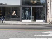 people walk past a building with windows displaying clothing stores and dresses on the sidewalk and car