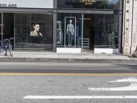 people walk past a building with windows displaying clothing stores and dresses on the sidewalk and car