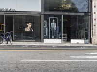 people walk past a building with windows displaying clothing stores and dresses on the sidewalk and car