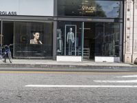 people walk past a building with windows displaying clothing stores and dresses on the sidewalk and car