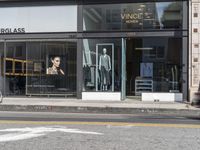 people walk past a building with windows displaying clothing stores and dresses on the sidewalk and car