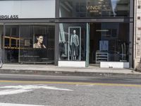 people walk past a building with windows displaying clothing stores and dresses on the sidewalk and car