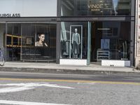 people walk past a building with windows displaying clothing stores and dresses on the sidewalk and car