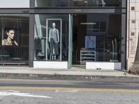 people walk past a building with windows displaying clothing stores and dresses on the sidewalk and car