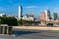 several barrels lined up on a roadway next to the city skyline and road with traffic