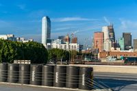 several barrels lined up on a roadway next to the city skyline and road with traffic