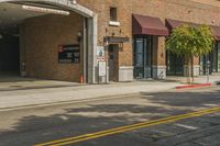 there are cars driving past this brick building in the city street way, and on the sidewalk, there is an outside building for a visitor parking area with a van