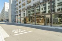 a paved street next to a building with glass windows with a logo on the side