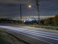 some long lines of light going along a roadway with power lines at night in the distance