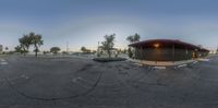 a fisheye lens image of an outdoor restaurant and parking lot with several trees and a fence