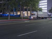 a truck driving down a city street in the night time at twilight with other cars and trees