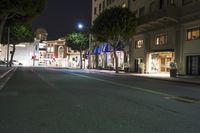 empty street in a city at night with cars on it and store lights lit up on the buildings