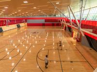 a gymnasium with large mirrors, basketball court and red walls and people walking around it