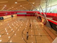 a gymnasium with large mirrors, basketball court and red walls and people walking around it