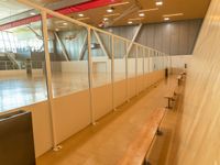 a line of benches inside a sports center next to a glass wall and ceiling filled with windows