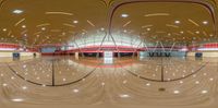 the inside of an indoor gym with a wooden floor and red seats, and the ceiling has two red stripes in each corner