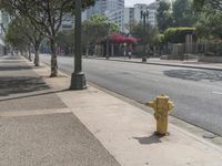 a yellow fire hydrant next to an empty sidewalk on a sunny day in a city