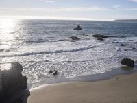 a view of a beach on a sunny day with a rocky shoreline and waves in the foreground