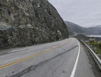 the road winds through a rocky valley on a cloudy day with mountains in the distance