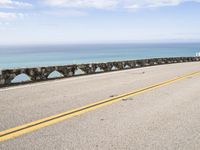 a man riding his motorcycle on a road next to the water with an ocean in the background