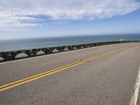 a man riding his motorcycle on a road next to the water with an ocean in the background