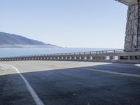 a road running next to a mountain that leads to the ocean with mountains in the background