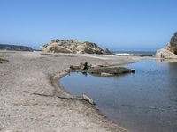 a water hole in the middle of a sandy beach with a rock and some birds on it