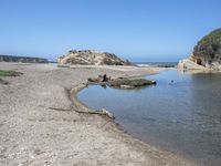 a water hole in the middle of a sandy beach with a rock and some birds on it