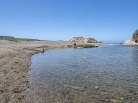 a water hole in the middle of a sandy beach with a rock and some birds on it