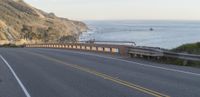 a scenic stretch of road on a cliff overlooking water and cliffs are pictured from a moving vehicle