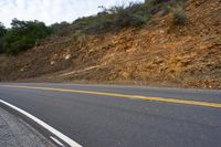 two yellow lines going into the ground next to an empty road with some hills in the background