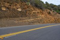 two yellow lines going into the ground next to an empty road with some hills in the background