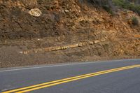 two yellow lines going into the ground next to an empty road with some hills in the background