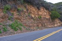 two yellow lines going into the ground next to an empty road with some hills in the background