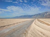 a long road running through an empty desert field with mountains in the background area in the distance, some trees line the edge