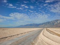 a long road running through an empty desert field with mountains in the background area in the distance, some trees line the edge