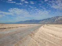 a long road running through an empty desert field with mountains in the background area in the distance, some trees line the edge