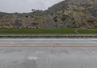 a car driving on an empty highway surrounded by mountains and hills with yellow curbing lines