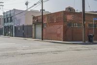 an empty street in front of a brick building with a car parked on the sidewalk