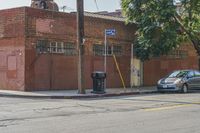 an empty street in front of a brick building with a car parked on the sidewalk