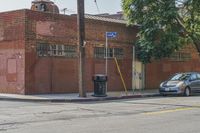 an empty street in front of a brick building with a car parked on the sidewalk