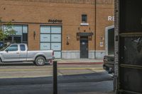 an empty street in front of a brick building with a car parked on the sidewalk