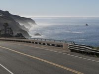 the empty highway is next to a rocky shoreline area and the ocean behind it the cliffs look like they're blown away